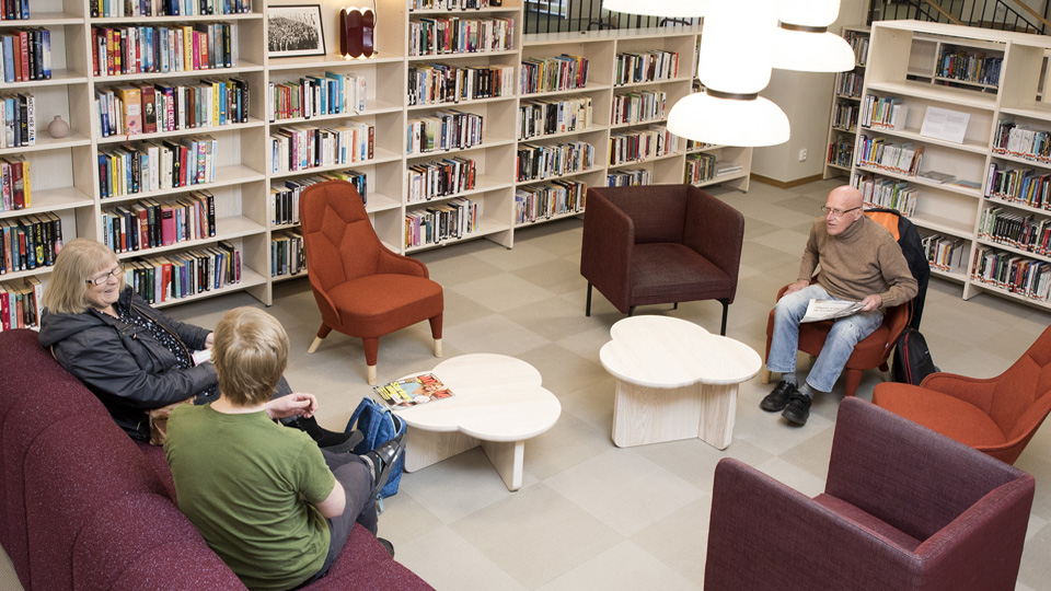 Tre personer sitter i soffor och fåtöljer i bibliotekets tidningshörna.