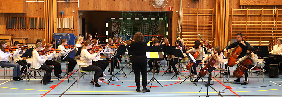 En stor orkester spelar på golvet i en gymnastiksal.