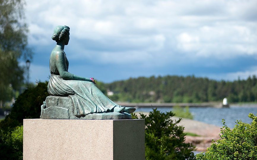 Fotografi av kvinnlig bronsskulptur som sitter ner och tittar ut mot vattnet. 