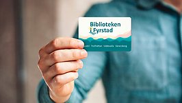 En person håller fram ett lånekort från Biblioteken i Fyrstad mot kameran.